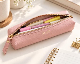 May include: A dusty pink, textured pencil case with a gold zipper closure. The name ALICE is embossed in gold on the front. The case is open, revealing several pens inside, including a pink pen, a yellow pen, and a white pen.
