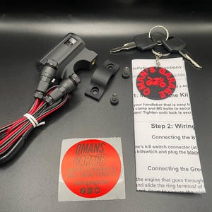 May include: A black motorcycle kill switch with wiring and a red and black wire. The switch is attached to a black handlebar clamp. The image also includes a red and black sticker with the text "OMANS GARAGE" and a red and black keychain with the text "OMAN'S GARAGE" and a motorcycle graphic. The image also includes instructions for installing the kill switch.