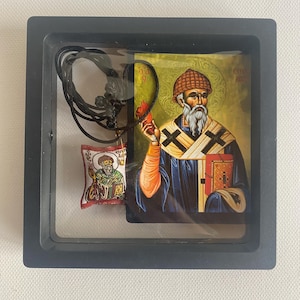 May include: A framed religious icon featuring a bearded figure in a blue robe, holding a book and a flame. A small pendant with a similar image and a black cord are also included. The frame is black.