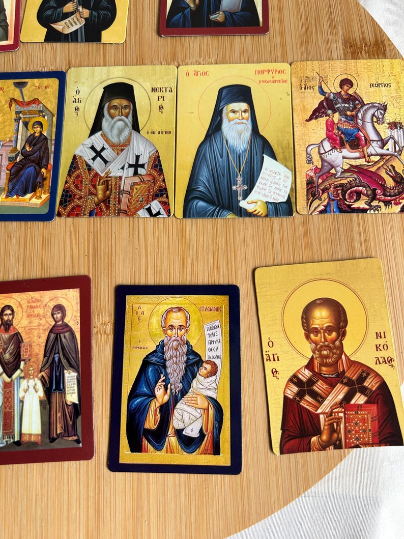 May include: A collection of religious icon cards featuring various saints and religious figures. The cards have gold backgrounds and depict figures in traditional attire, with some holding books or scrolls. The images are colorful and detailed.