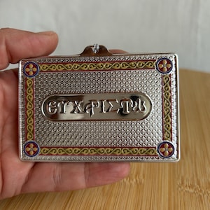 May include: A rectangular silver-toned metal plaque featuring a textured diamond pattern and a central horizontal panel with the Greek text "ΕΥΧΑΡΙΣΤΩ". The border is decorated with gold and red scrollwork and four circular blue and red floral motifs.
