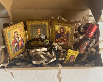 May include: A collection of religious icons, a rosary, and a small bottle of perfume inside a cardboard box. The icons feature images of religious figures. The box is filled with brown paper filler.