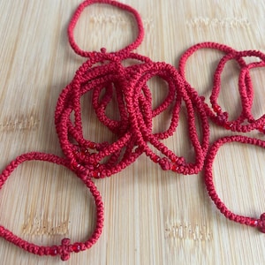 Könnte beinhalten: Ein Stapel roter Armbänder aus Schnur mit kleinen roten Perlen. Die Armbänder sind geknüpft und haben ein schlichtes Design.