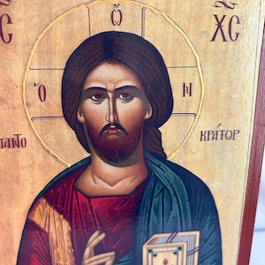 Może przedstawiać: Ikona religijna przedstawiająca Jezusa Chrystusa trzymającego książkę. Ikona jest namalowana w tradycyjnym stylu ze złotymi akcentami i czerwonym tłem. Tekst "XC" jest widoczny w prawym g&oacute;rnym rogu ikony.