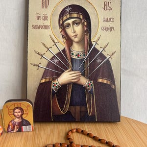 Puede incluir: Un icono religioso que representa a la Virgen María con siete espadas que le atraviesan el corazón. El icono está pintado en un panel de madera y tiene un fondo dorado. El texto en el icono dice "Пре св. Умаление" y "Залих Сердец".