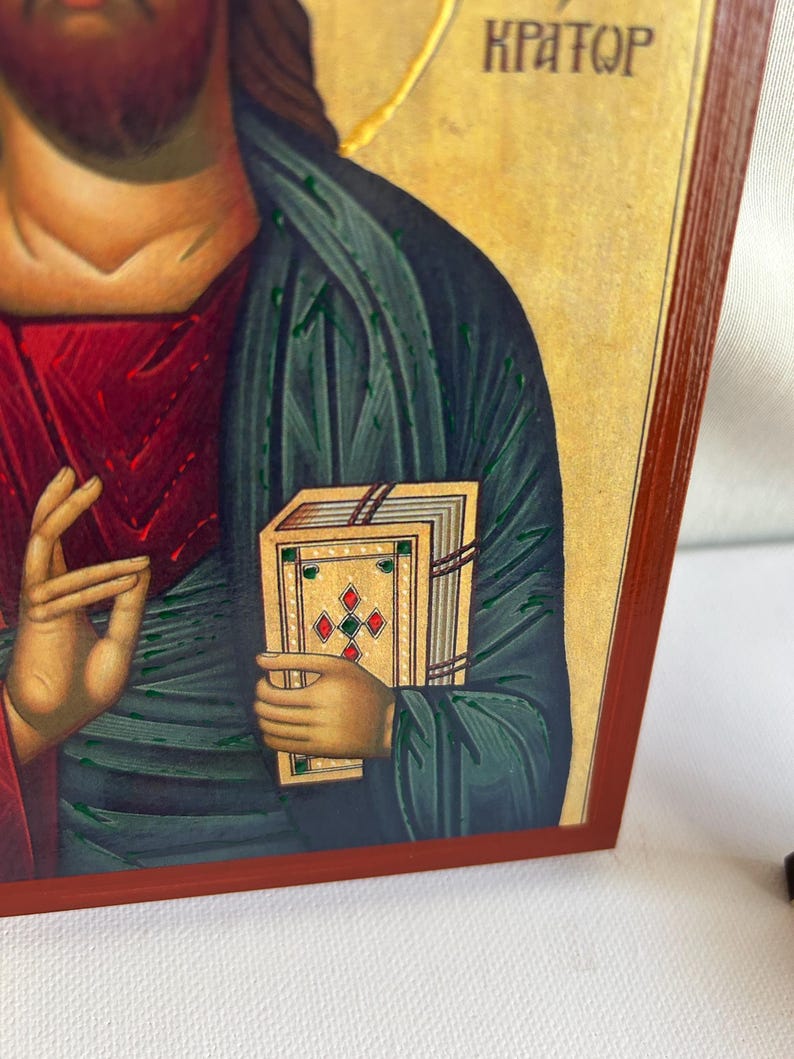 Może przedstawiać: Ikona religijna przedstawiająca Jezusa Chrystusa trzymającego książkę z napisem "KPATOQ" nad nim. Ikona jest namalowana w tradycyjnym stylu z żywymi kolorami i misternymi detalami.