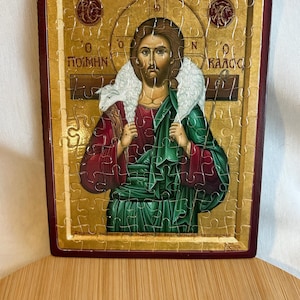 Puede incluir: Un rompecabezas enmarcado que representa un icono religioso de Jesucristo como el Buen Pastor. El icono está pintado en un estilo bizantino tradicional con acentos dorados. El texto "O  POIMHN O KALOS" está escrito en griego en la parte superior de la imagen.