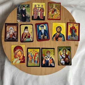 May include: A collection of religious icons featuring various saints and biblical scenes. The icons are rectangular with gold, red, and blue accents, arranged on a round wooden surface. The images depict figures in traditional attire.