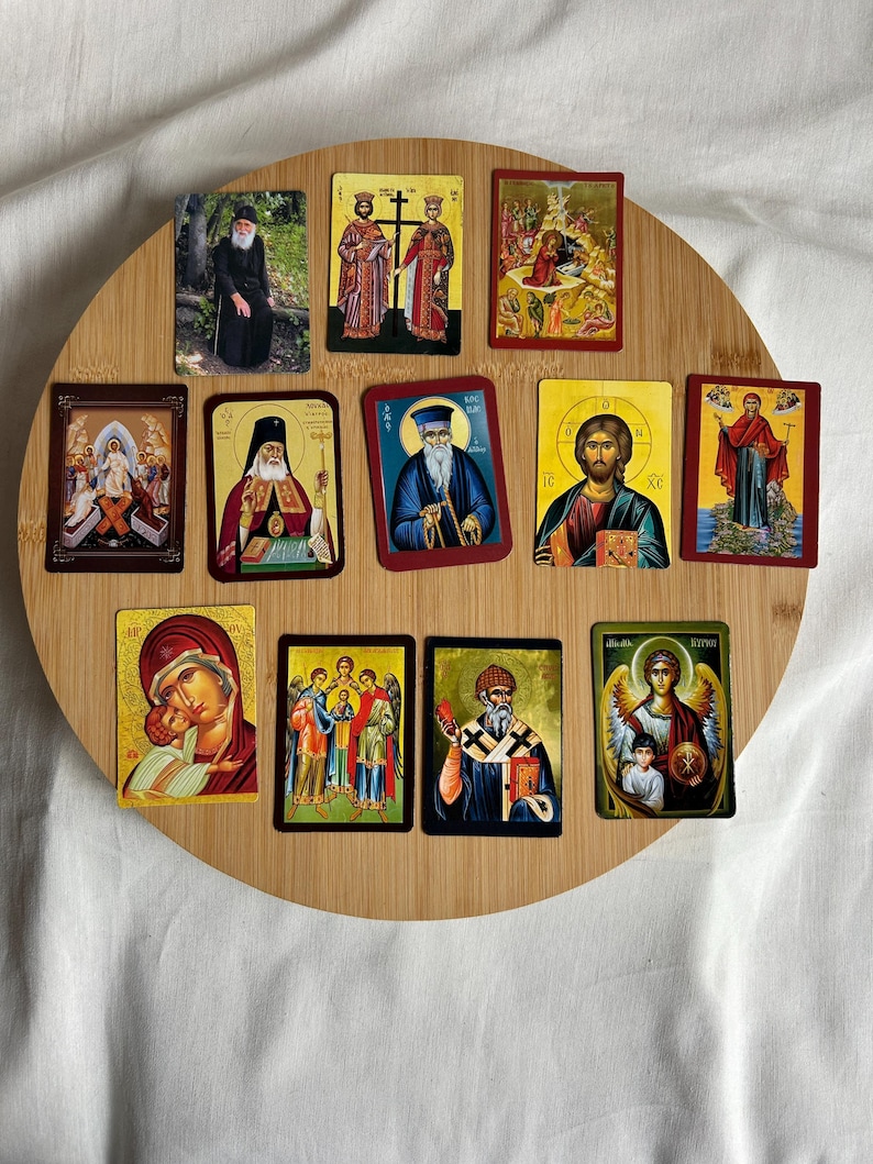May include: A collection of religious icons featuring various saints and biblical scenes. The icons are rectangular with gold, red, and blue accents, arranged on a round wooden surface. The images depict figures with halos and traditional religious attire.