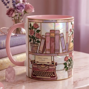 May include: A ceramic mug with a pink handle and rim, featuring a design of books, roses, and a typewriter. The mug has a capacity of 11 oz. The design is in shades of pink, white, and gold, with the words "Once upon a time..." on the mug.