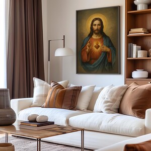 May include: A framed religious portrait depicts a figure with long hair, a halo, and a heart symbol. The figure wears a blue and red robe. The artwork hangs above a white sofa with decorative pillows in a living room setting.