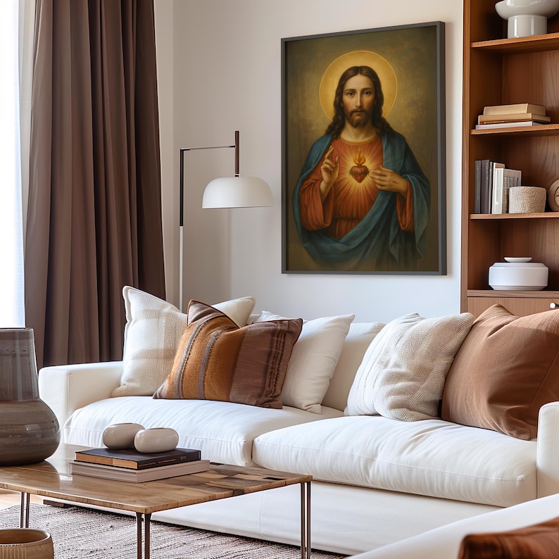 May include: A framed religious portrait depicts a figure with long hair, a halo, and a heart symbol. The figure wears a blue and red robe. The artwork hangs above a white sofa with decorative pillows in a living room setting.