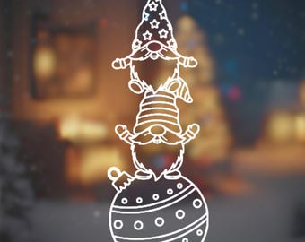 Op de afbeelding: Witte lijntekening van drie kabouters gestapeld op een kerstbal. De bovenste kabouter draagt een hoed met sterren, de middelste kabouter heeft een gestreepte hoed en de onderste kabouter staat op een versierde bal.