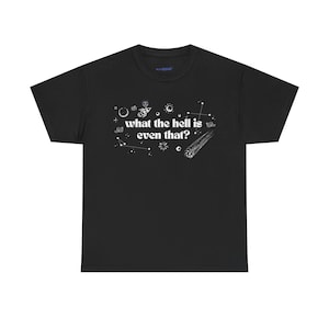 Peut inclure: T-shirt noir avec un motif blanc représentant des éléments célestes tels que des planètes, des étoiles et une comète. Le texte "what the hell is even that?" est imprimé.