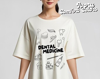 Op de afbeelding: Ivoor kleurig T-shirt met korte mouwen met een zwart lijntekening ontwerp van tandheelkundige instrumenten en tanden. De woorden "DENTAL MEDICINE" zijn gedrukt in vette zwarte letters. De tekst "Ivory Comfort Colors" is gedrukt in een scriptlettertype.