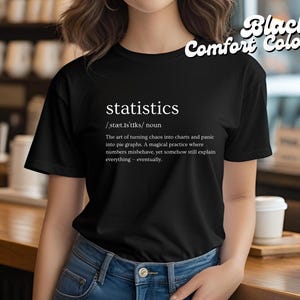 May include: Black t-shirt with the word "statistics" and its definition printed in white. The definition describes statistics as turning chaos into charts and panic into pie graphs. The shirt also has "Black Comfort Colors" printed on it.