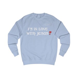 Könnte beinhalten: Hellblaues Sweatshirt mit dem weißen Schriftzug "I'M IN LOVE WITH JESUS!". Das Design beinhaltet eine kleine Auto- und Herzgrafik. Ein rotes Herz befindet sich neben dem Ausrufezeichen.