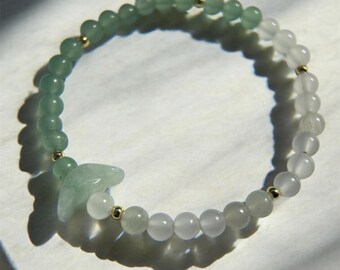 May include: A green and white beaded bracelet with a jade charm. The bracelet is made with small, round beads and has a gold accent.