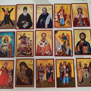 Puede incluir: Una colección de catorce iconos religiosos rectangulares que representan a varios santos, figuras bíblicas y seres divinos. Cada icono muestra ilustraciones detalladas con fondos dorados, ropa ornamentada e inscripciones en griego o cirílico.