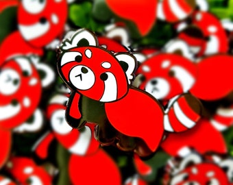Könnte beinhalten: Eine Nahaufnahme einer roten Panda-Emaille-Anstecknadel. Die Anstecknadel hat die Form eines roten Panda-Cartoons mit weißen Markierungen. Die Anstecknadel ist von anderen roten Panda-Anstecknadeln umgeben, die alle unscharf sind.
