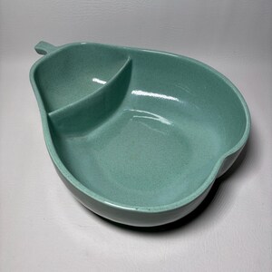 May include: A vintage, pear-shaped serving dish in a speckled, seafoam green color. The dish is divided into two sections, with a small handle-like extension at the top. The dish is likely made of ceramic or a similar material.
