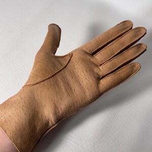 K&ouml;nnte beinhalten: Hellbrauner Lederhandschuh mit strukturierter Oberfl&auml;che und dekorativen N&auml;hten. Der Handschuh ist im klassischen F&uuml;nf-Finger-Stil gehalten und zeigt eine Vintage-&Auml;sthetik.