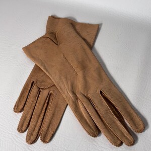 K&ouml;nnte beinhalten: Ein Paar hellbraune Lederhandschuhe. Die Handschuhe sind aus weichem, strukturiertem Leder gefertigt und weisen detaillierte N&auml;hte entlang der N&auml;hte und um die Finger auf. Die Handschuhe sind in einem klassischen, eleganten Stil gehalten.
