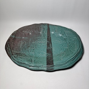 Puede incluir: Plato ovalado de cerámica con diseño de hojas. El plato está dividido en dos secciones, una en color marrón oscuro y otra en color turquesa. El diseño de hojas está en relieve en la superficie.