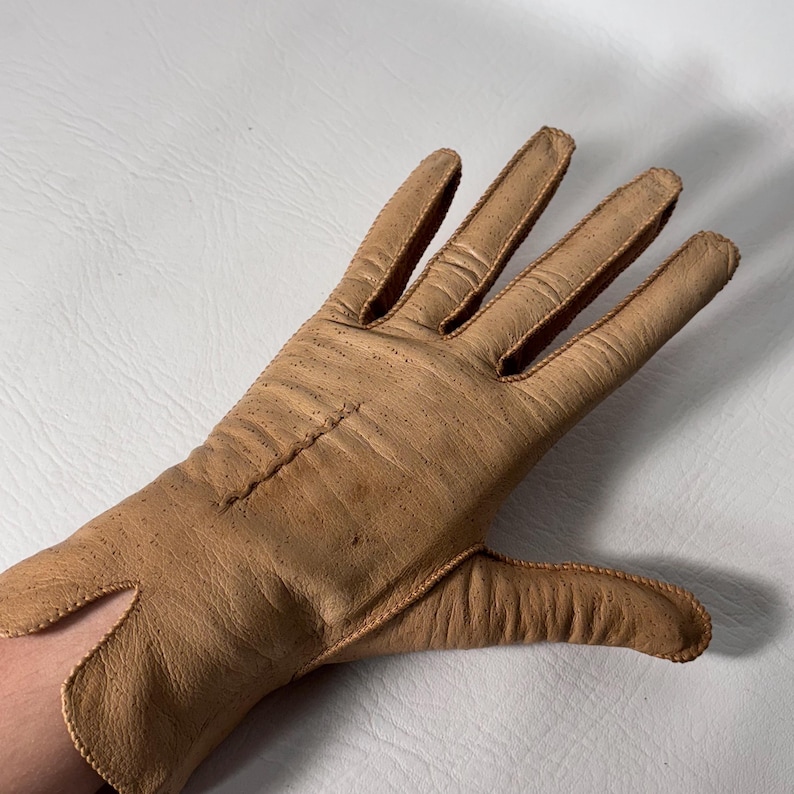 K&ouml;nnte beinhalten: Ein hellbrauner Lederhandschuh mit sichtbaren N&auml;hten und einer strukturierten Oberfl&auml;che. Der Handschuh hat ein klassisches Design mit einzelnen Fingerschlitzen und einer Handgelenks&ouml;ffnung. Der Handschuh ist wahrscheinlich Vintage.