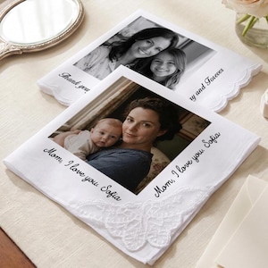 Op de afbeelding: Twee witte stoffen zakdoeken met geschulpte randen, elk voorzien van een zwart-wit afgedrukte foto van een persoon die een baby vasthoudt. De voorste zakdoek bevat de gedrukte tekst Mom, I love you. Sofia en een wit kanten hoekdetail.