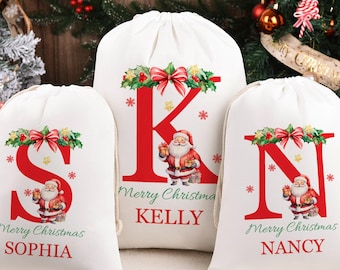 May include: Three white drawstring Christmas gift bags with red letters, Santa Claus illustrations, and the words "Merry Christmas" and names. The bags are decorated with festive greenery and bows.