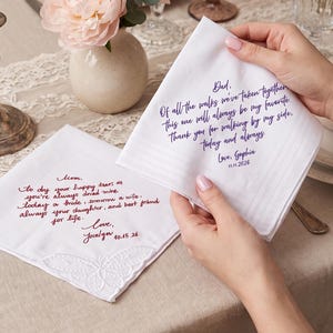 May include: Two white fabric handkerchiefs with embroidered text. One features purple script text addressed to Dad with a date of 11.15.2026. The other features red script text addressed to Mom with a date of 10.15.26 and a white butterfly motif.
