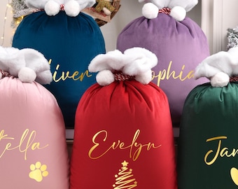 May include: Five velvet Christmas gift sacks in pink, dark blue, purple, red, and dark green. Each sack features a white plush top with pom-poms, a drawstring closure, and gold foil lettering displaying names like Stella, Evelyn, and James.