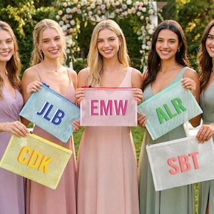 May include: Five women in pastel dresses hold mesh zipper pouches with initials. The pouches are in various colors: blue, pink, green, yellow, and white. The background features greenery and a floral arch.