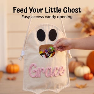 Puede incluir: Una bolsa de dulces de lona color crema con forma de fantasma, ojos de fieltro negro y una abertura central. El nombre Grace est&aacute; bordado en hilo rosa en el frente. La bolsa tiene un asa de cuerda blanca y el texto Feed Your Little Ghost.