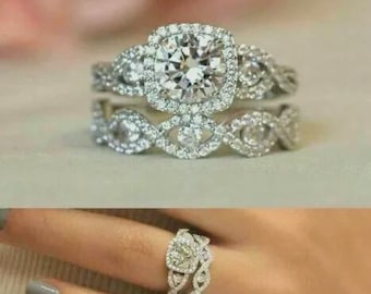 May include: A set of two silver rings with clear, sparkling stones. The engagement ring features a large, square-cut center stone surrounded by smaller stones. The wedding band has an intertwined design with additional stones.