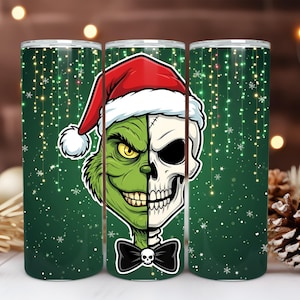 May include: A green and white tumbler featuring a half-Grinch, half-skull design wearing a Santa hat and a black bow tie. The background is a dark green with falling snowflakes and sparkling lights. A festive holiday theme.