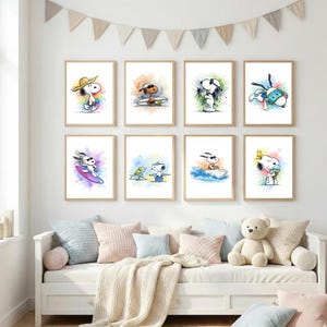 Puede incluir: Una colección de ocho láminas enmarcadas de Snoopy. Cada lámina presenta a Snoopy en diversas actividades veraniegas, como surfear y tomar el sol, con coloridos fondos de acuarela. Las láminas se exhiben sobre un diván blanco con cojines y un oso de peluche.