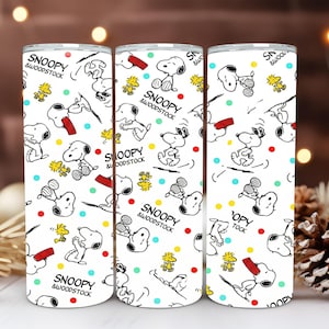 May include: Three white tumblers with a repeating pattern of Snoopy and Woodstock cartoon characters in black and yellow. The tumblers have the text "Snoopy & Woodstock" and are decorated with colorful dots.