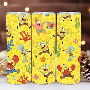 Op de afbeelding: Gele beker met een herhaald patroon van SpongeBob SquarePants, Patrick Star, Octo Tentakel en Mr. Krabs. Het ontwerp bevat koraal, zeewier en bloemen. De beker is cilindrisch en heeft een zilveren boven- en onderkant.