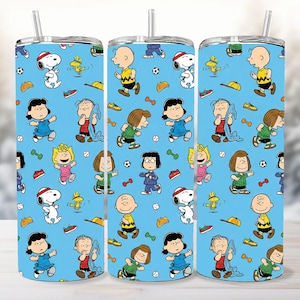 Puede incluir: Tres vasos azules con un patrón repetido de personajes de dibujos animados, incluyendo a Snoopy, Charlie Brown y Lucy. El diseño presenta equipos y accesorios deportivos. Cada vaso tiene una tapa plateada y una pajita.