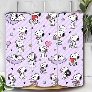 Puede incluir: Tres vasos de acero inoxidable con un patrón repetido de personajes de Snoopy en varias poses sobre un fondo morado claro con rayas diagonales. El diseño incluye corazones, flores y Snoopy sosteniendo objetos.