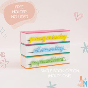May include: A multi-layered book holder with three phrases: "go away to reading", "not now I'm busy", and "you promised here". The holder is white with pink, green, and orange accents. The text "FREE HOLDER INCLUDED" is also visible.