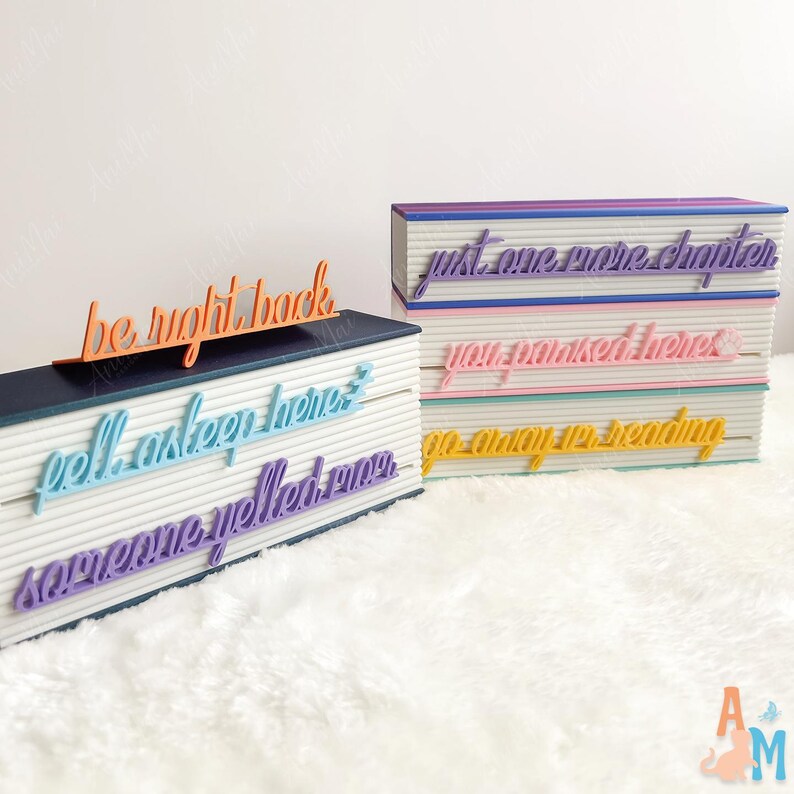 May include: Decorative book-shaped objects with colourful text. One has "be right back" in orange. Another has "fell asleep here", and "someone yelled omg" in blue and purple. The other has "just one more chapter", "you marked here", and "go away I'm reading".