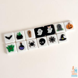 May include: A collection of fourteen square tiles featuring raised Halloween-themed icons including a black bat, green cauldron, brown coffin, white ghosts, gray tombstone, orange pumpkin, green monster, purple potion, black spider, skull, web, and hat.