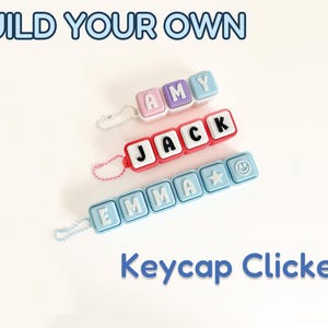 May include: Three custom keycap clicker keychains with small ball chains. The top one is pink and blue with the name AMY. The middle one is red with the name JACK. The bottom one is light blue with the name EMMA, a star, and a smiley face icon.