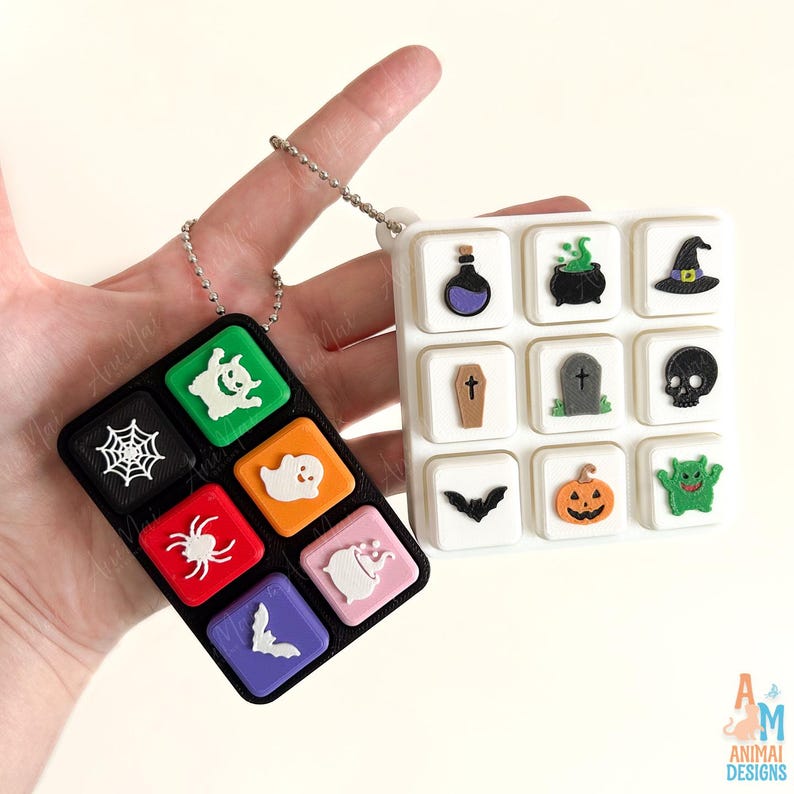 May include: Two rectangular keychains featuring a grid of raised Halloween-themed icons. The black keychain displays a white spiderweb, ghost, spider, bat, and green monster. The white keychain features a potion, cauldron, hat, coffin, tombstone, skull, bat, pumpkin, and green monster.