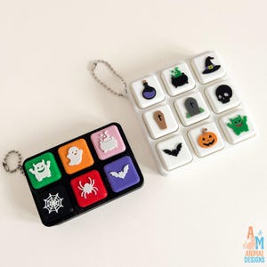 May include: Two rectangular keycap sets with Halloween-themed icons. The black set features a green monster, white ghost, pink cauldron, black spiderweb, red spider, and purple bat. The white set includes a potion, cauldron, hat, coffin, tombstone, skull, bat, pumpkin, and green monster.
