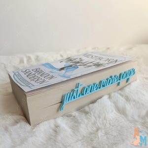 K&ouml;nnte beinhalten: Ein Buch mit dem Titel "Mistborn" von Brandon Sanderson mit einem hellblauen Lesezeichen mit der Aufschrift "just one more page". Das Buch hat ein hellblaues und wei&szlig;es Cover-Design. Das Lesezeichen besteht aus hellblauem Material.