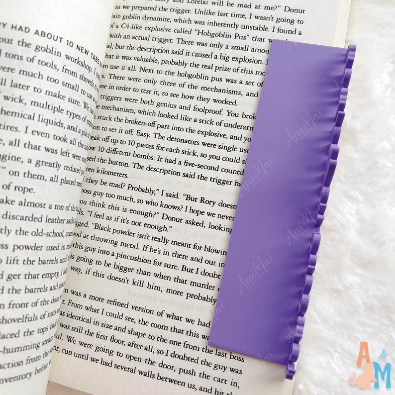 May include: A lilac bookmark with a frilled edge, lying on an open book. The bookmark is rectangular and made of a flexible material. The book's pages display printed text.